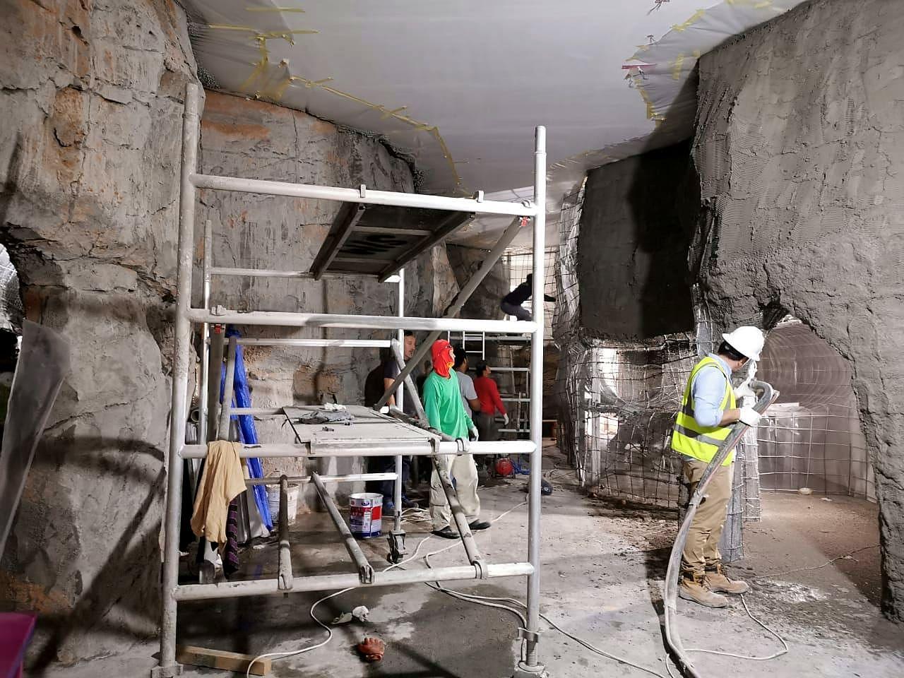 Crews sculpting artificial rock walls for an immersive cave environment.