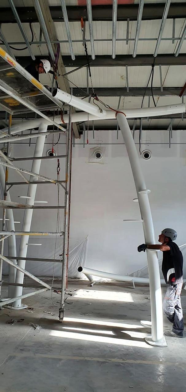 Workers in safety helmets raising curved white steel tree structures.