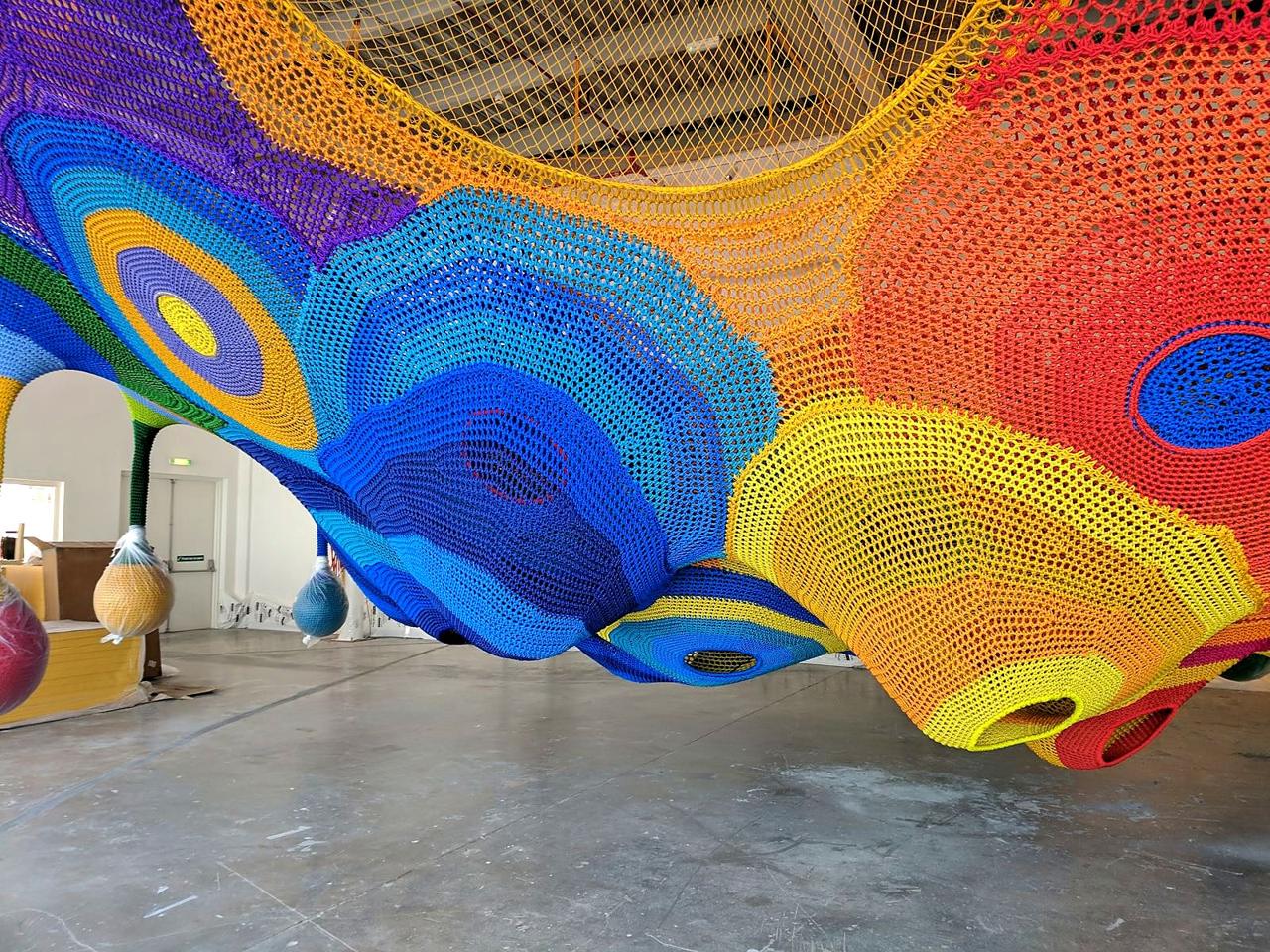 A colourful crochet net climbing structure being installed before opening.