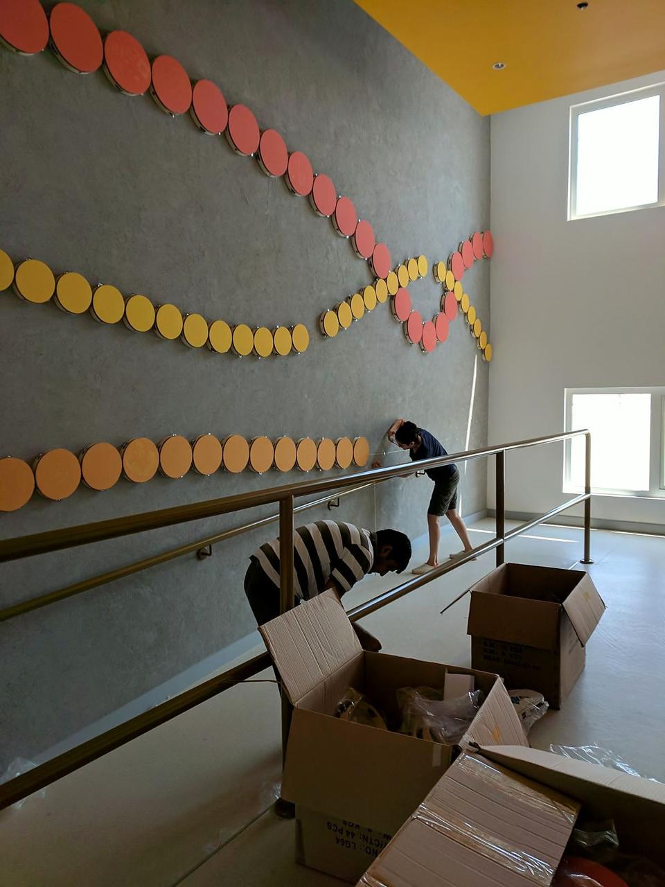 Installers mounting a wall of colourful tambourines along a ramp.