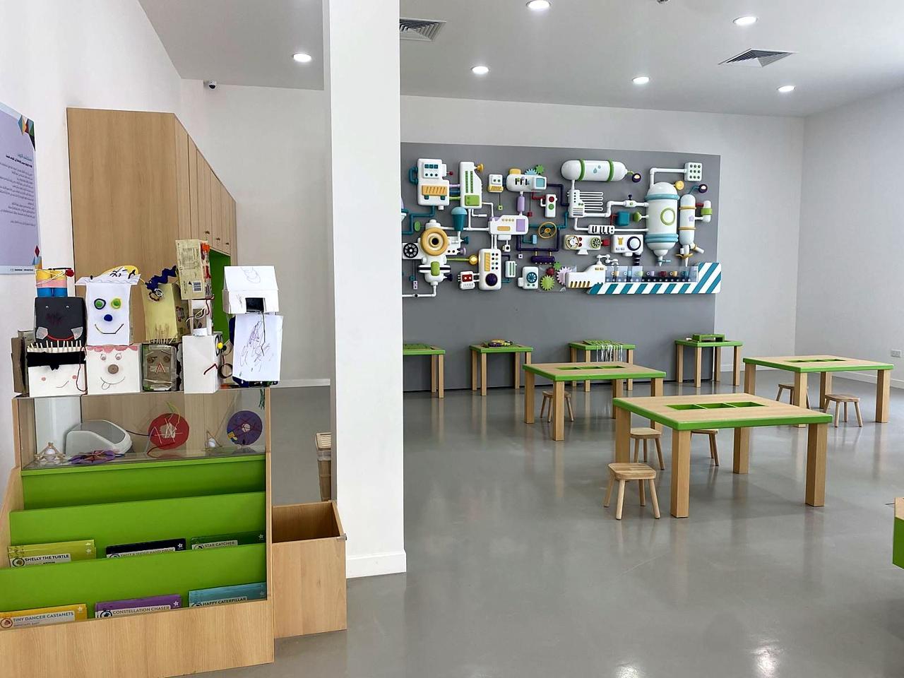 A finished making studio with low green tables and a colourful interactive machine wall.