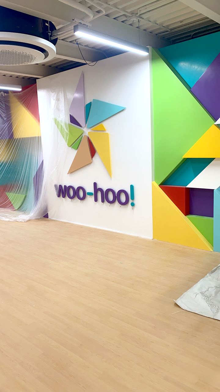 The woo-hoo! logo wall freshly installed beside colourful geometric panels.
