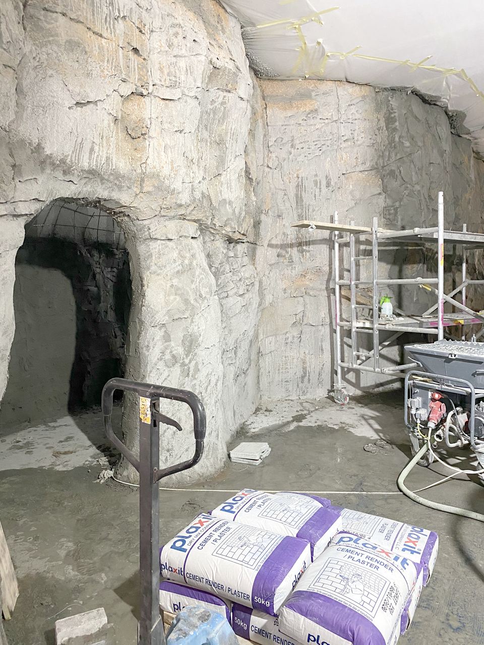 Sculpted cave walls taking shape, with plaster bags and a rendering machine on site.