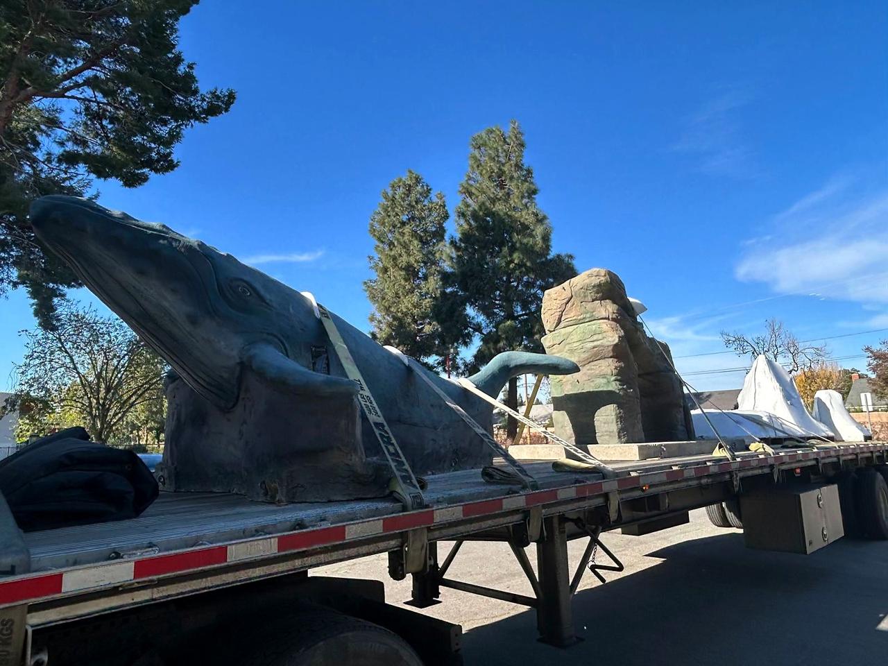 A life-size whale sculpture and rock forms strapped to a flatbed truck for delivery.