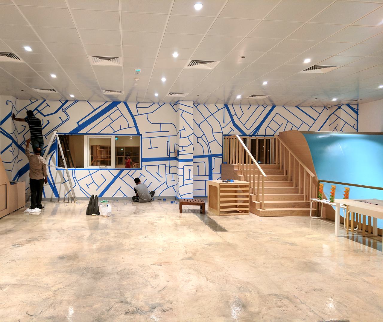 Installers taping a blue street-map mural across a gallery wall before opening.
