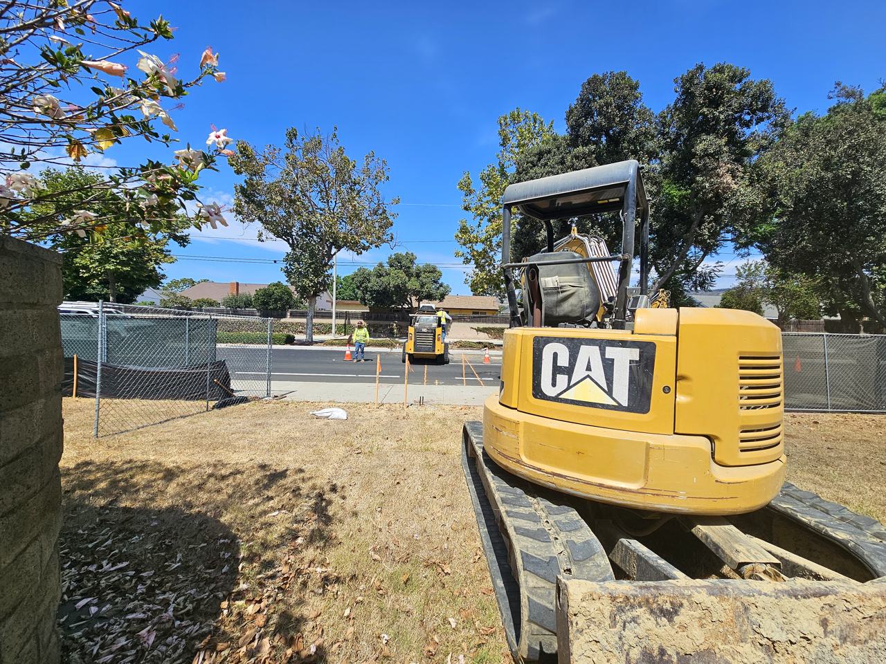 A compact excavator on site while crews mark out the street during early construction.