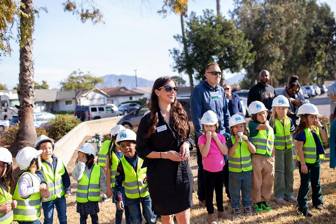 Dani Hildreth smiling among children in hard hats and safety vests at the kidSTREAM groundbreaking.