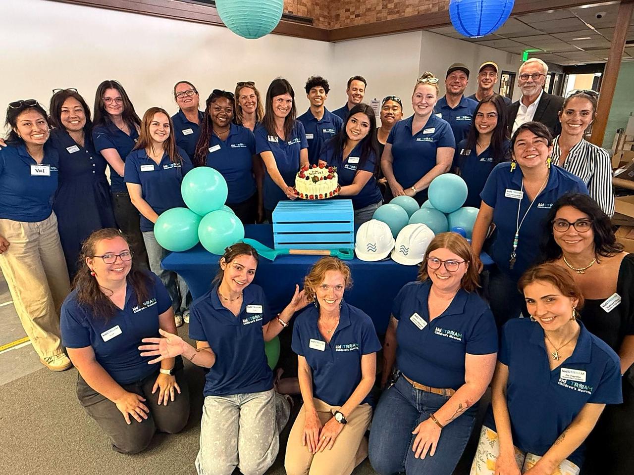 The kidSTREAM team in matching polos gathered around a celebration cake.