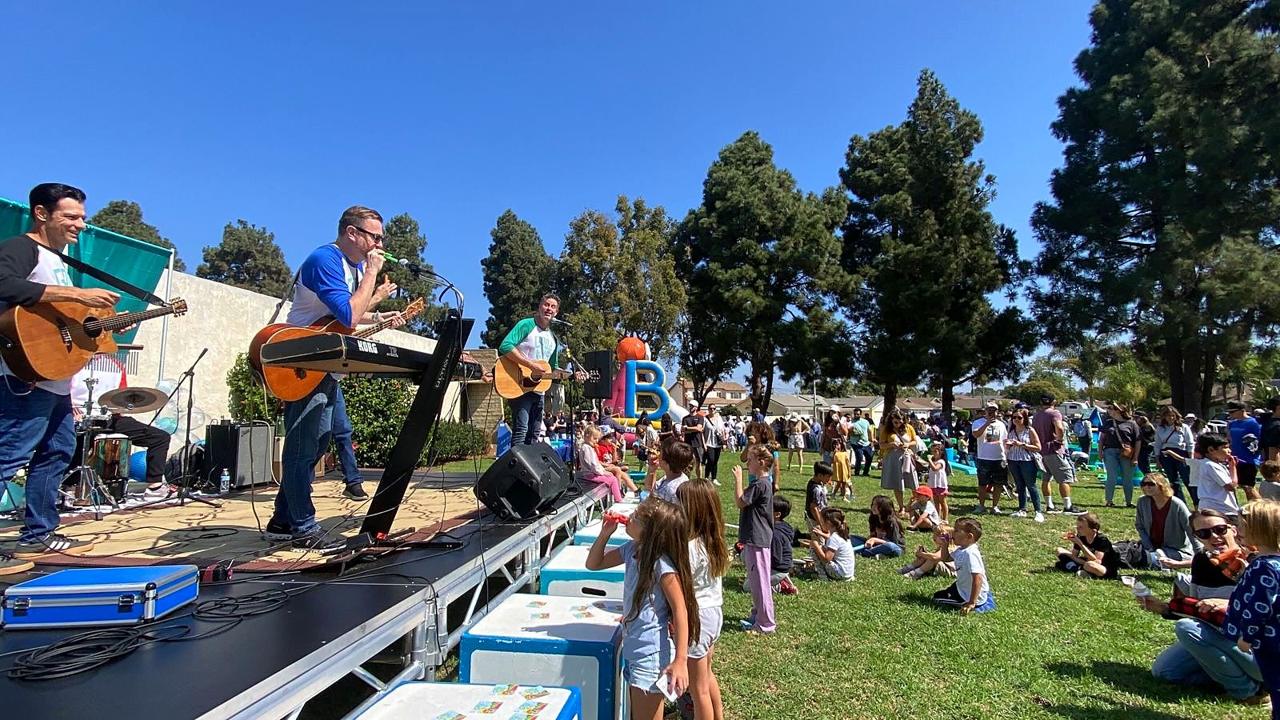 A family band performing on stage for children dancing on the grass.