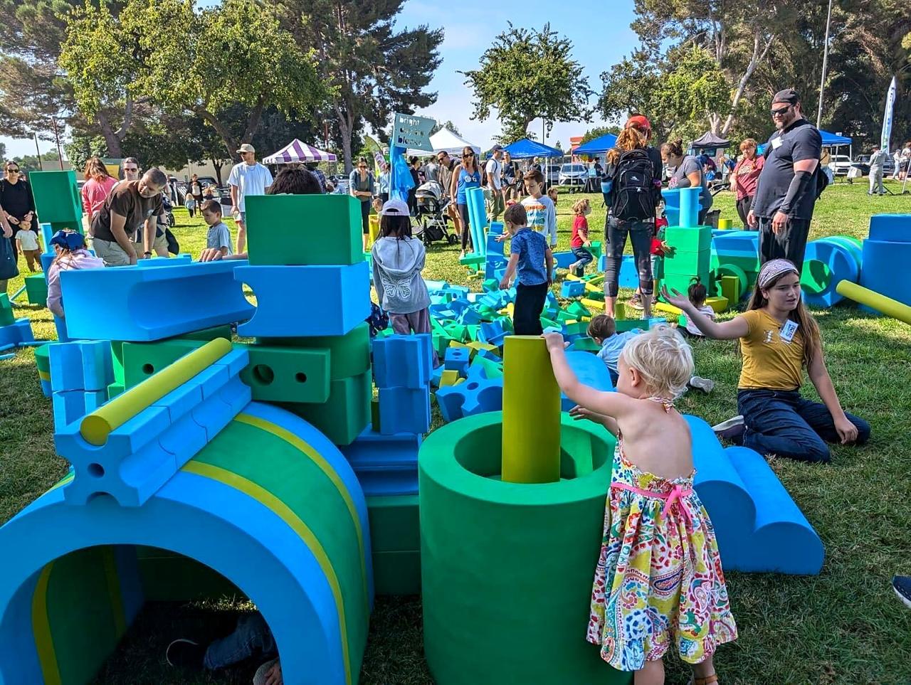 Children building with giant blue and green foam blocks at an outdoor festival.