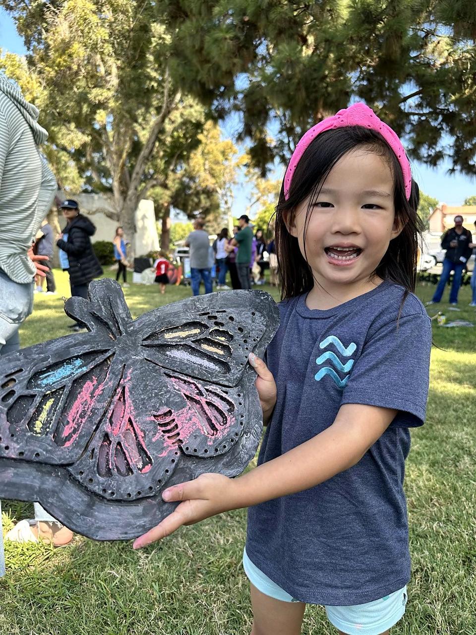 A smiling girl holding up her chalk butterfly rubbing.