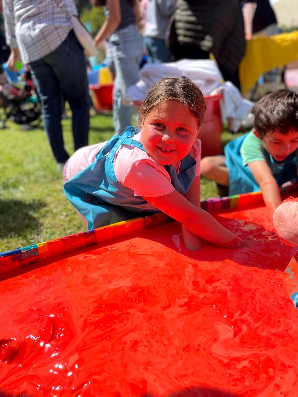 A girl in an apron with her arm deep in a tub of bright orange slime.