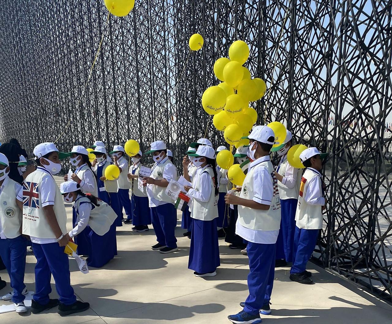School groups with yellow balloons and flags at an Expo 2020 Dubai celebration.