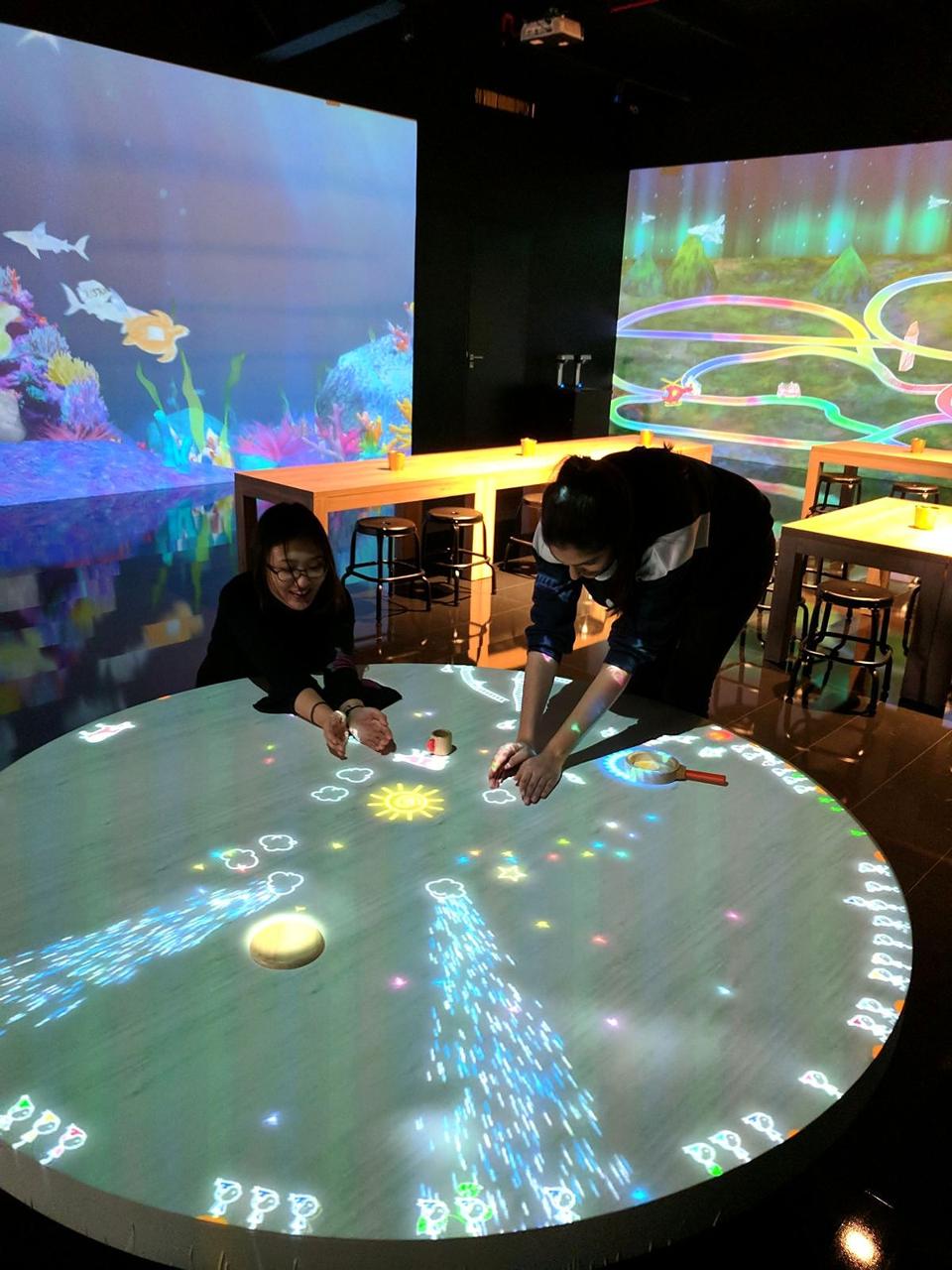 Two team members testing an interactive projection table in an immersive gallery.