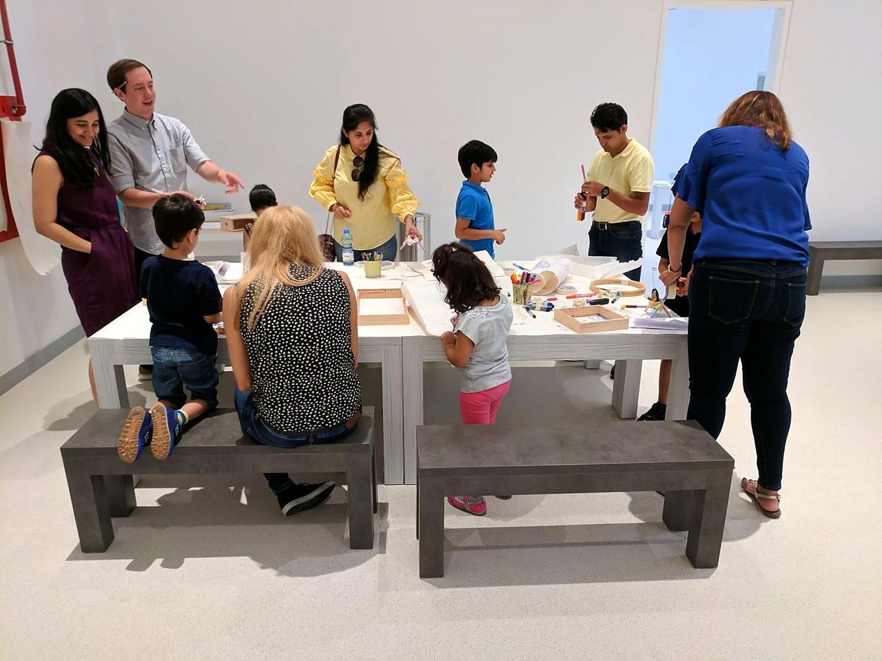 Families and an educator around a making table in a bright studio workshop.