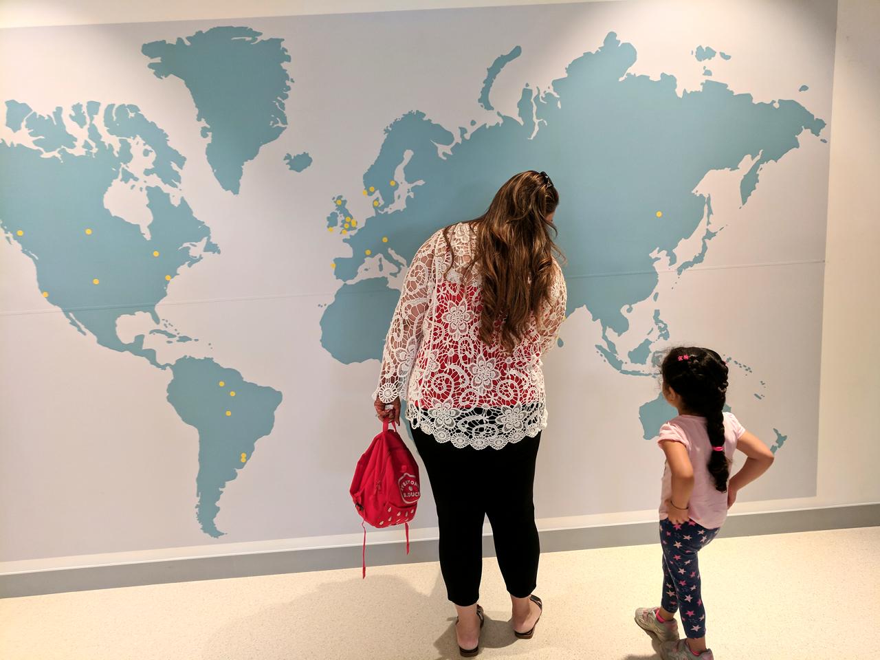 A mother and daughter exploring a large world map wall together.