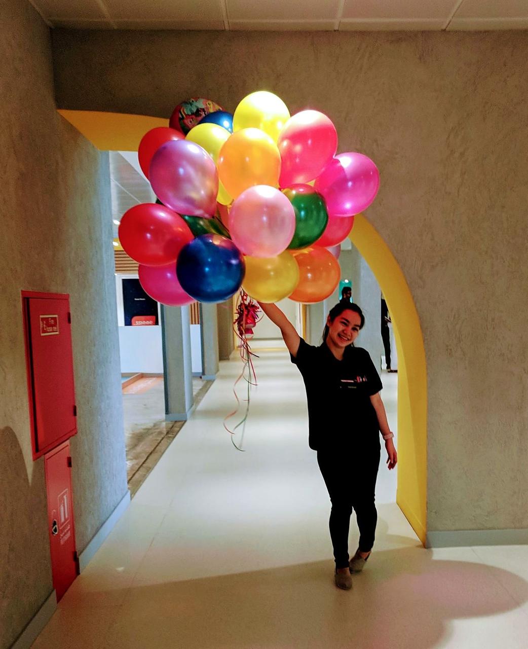 A smiling team member carrying a big bunch of balloons through a museum corridor.