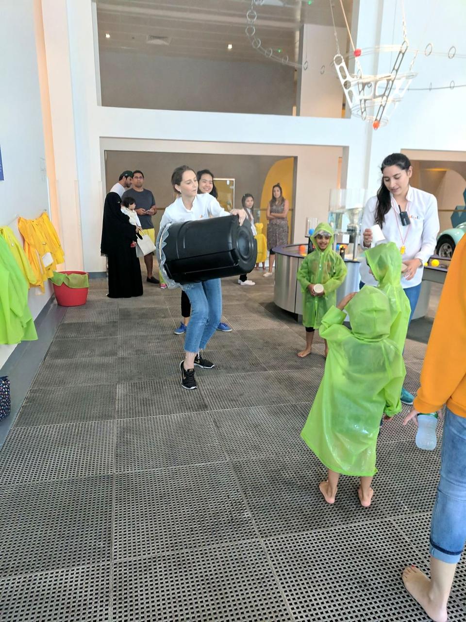 Educators running a water-play demonstration for children in green raincoats.