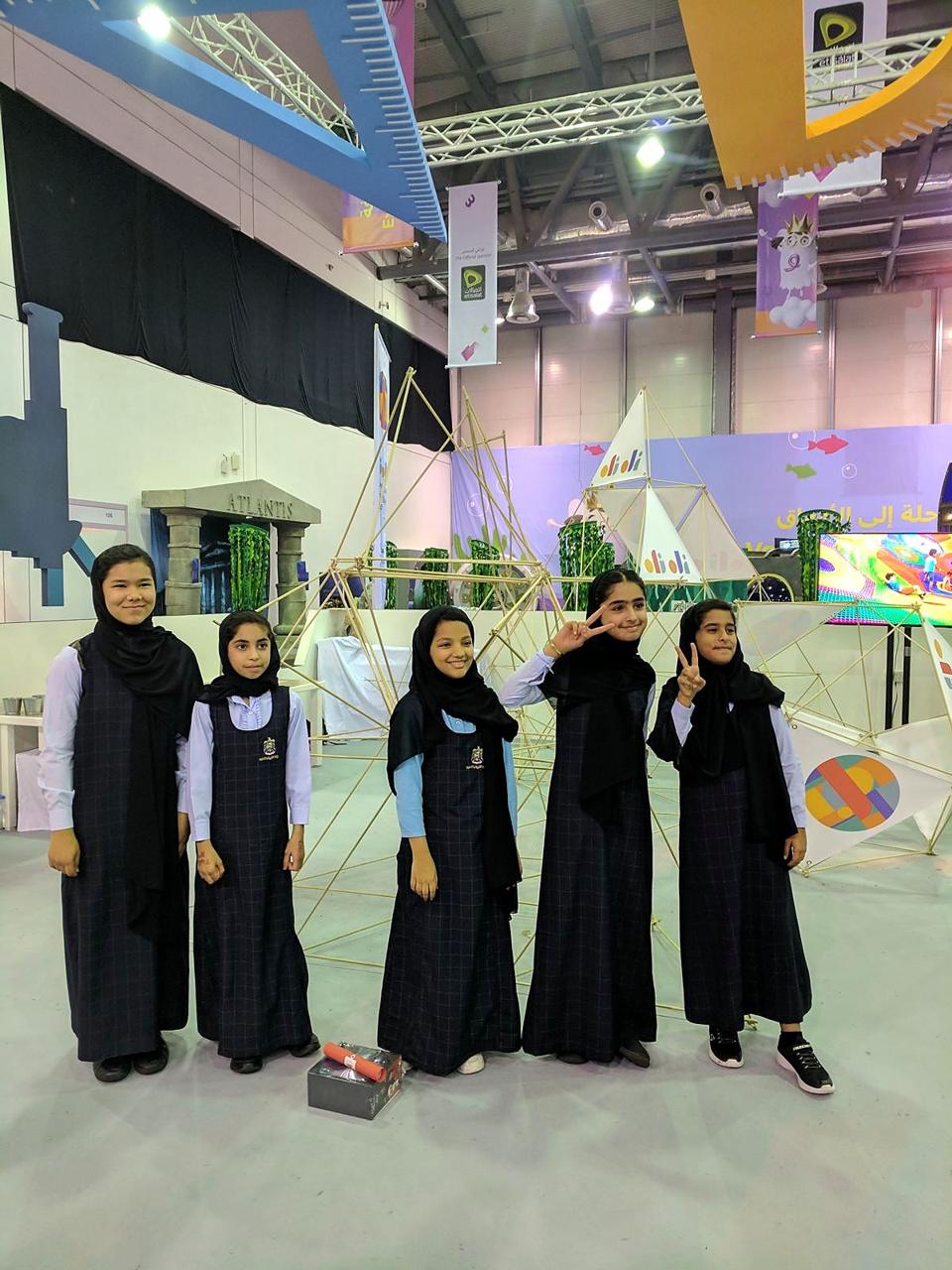 Schoolgirls posing proudly in front of a bamboo geodesic structure at the OliOli festival stand.