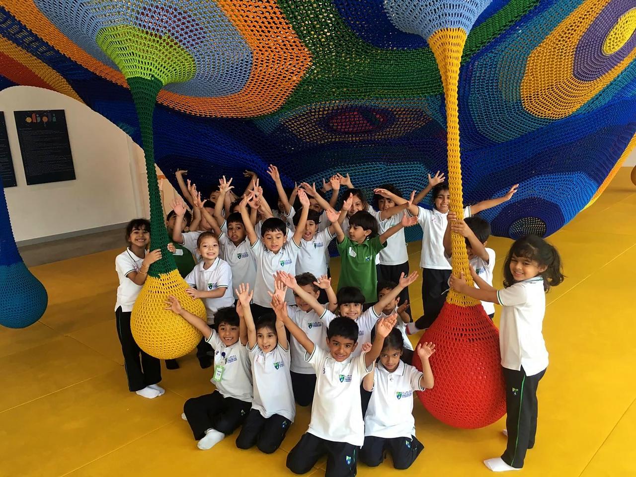 A school group cheering beneath the colourful crochet net climbing structure.
