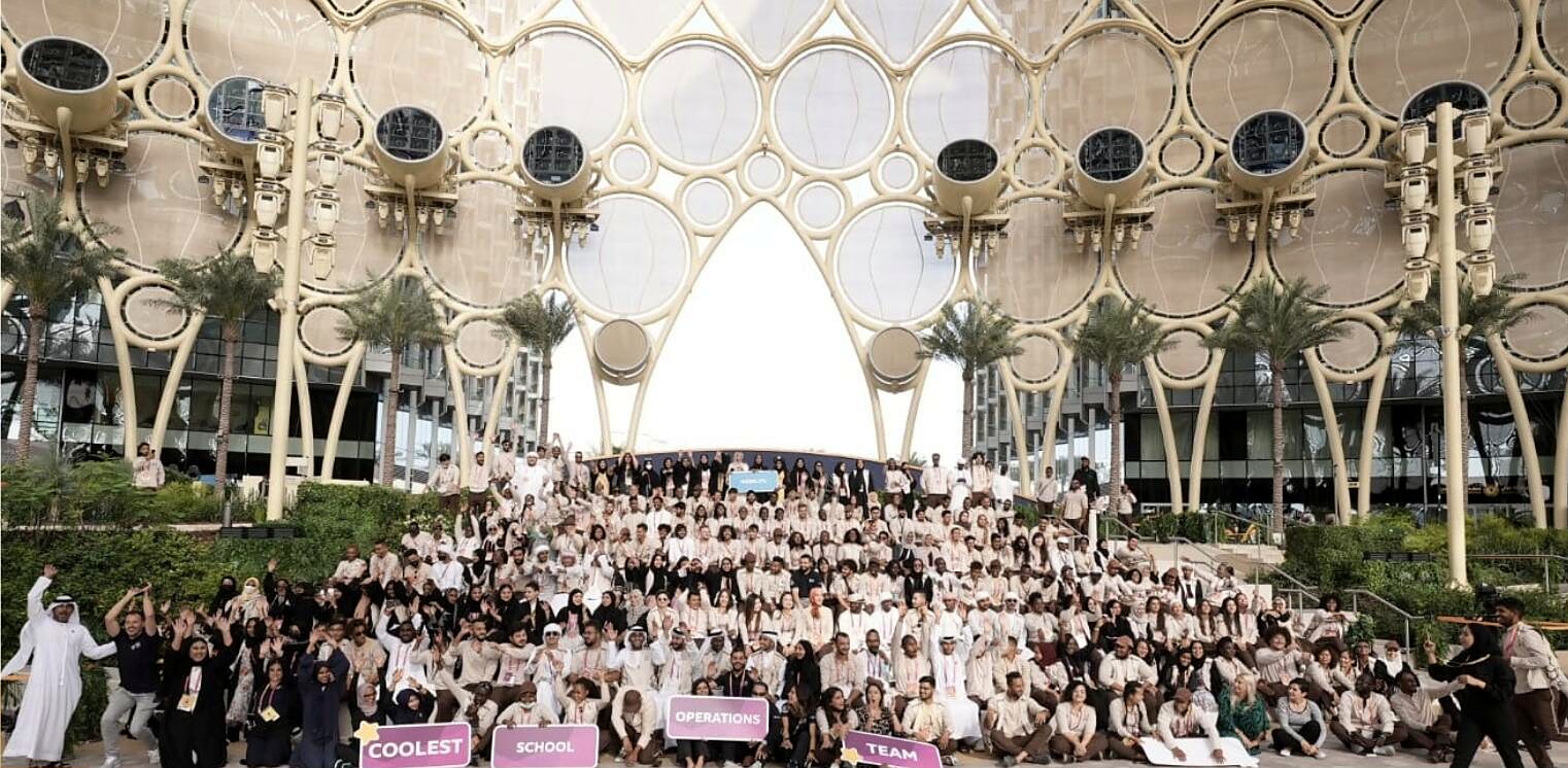 Dani's Expo 2020 Dubai School Operations team gathered beneath the Al Wasl dome, holding signs that read Coolest School Operations Team.